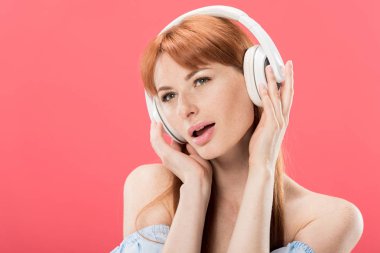 çekici kızıl saçlı kadın kulaklık müzik dinleme ve uzak pembe izole bakıyor