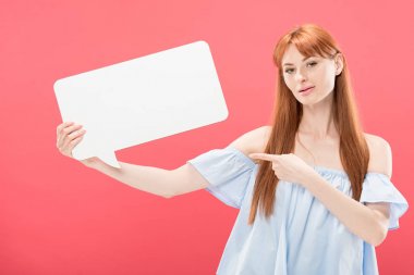 redhead genç kadın boş konuşma balonu parmak ile işaret ve pembe izole kamera bakıyor