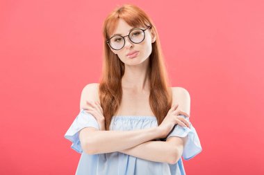 gözlük ciddi kızıl saçlı kız ön görünümü çapraz kolları ile ayakta ve kamera pembe izole bakarak