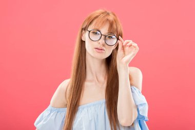 meraklı kızıl saçlı kadının ön görünümü kameraya bakıyor ve pembe izole gözlük dokunmadan