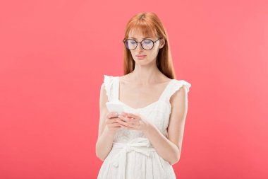 gözlük ve beyaz elbiseli redhead kadın pembe izole akıllı telefon kullanarak