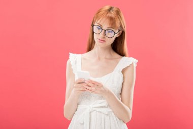 gözlük ve beyaz elbiseli redhead kadın pembe izole akıllı telefon kullanarak