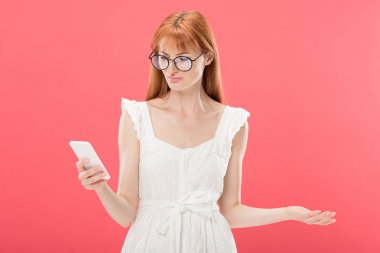 gözlük ve beyaz elbiseli kırmızı saçlı genç kadın pembe izole akıllı telefon kullanarak