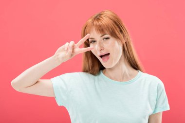 t-shirt çekici kızıl saçlı kız gülümseyerek ve pembe izole barış işareti gösteren