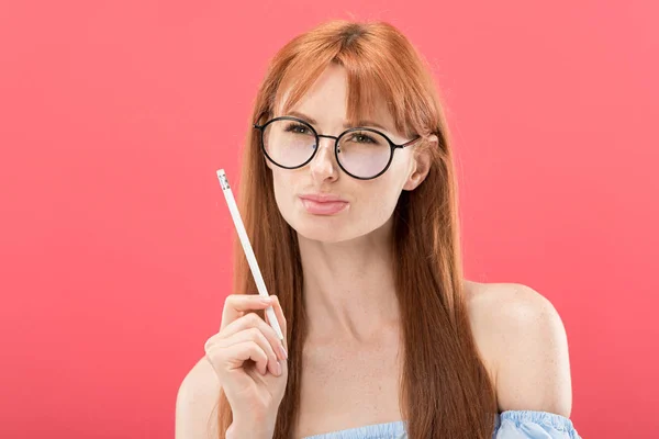 ピンクに隔離された鉛筆を持つ眼鏡をかけた赤毛の若い女性 — ストック写真