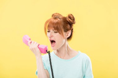 stressed redhead young woman holding handset and screaming isolated on yellow clipart