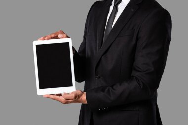 gri izole boş ekran ile dijital tablet gösteren siyah takım elbiseli işadamının kırpılmış görünümü