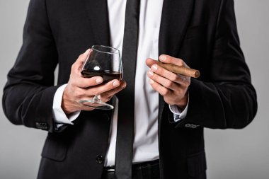 gri izole viski ve puro ile cam tutan siyah takım elbiseli işadamı kısmi görünümü