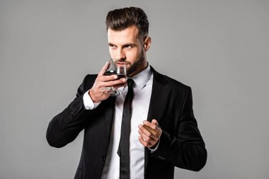 siyah takım elbiseli yakışıklı işadamı gri izole viski içme