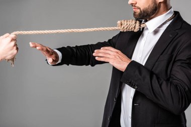 boynunda ilmik olan siyah takım elbiseli işadamının kırpılmış görünümü gri üzerinde izole halat ile katile dur jesti gösteriyor