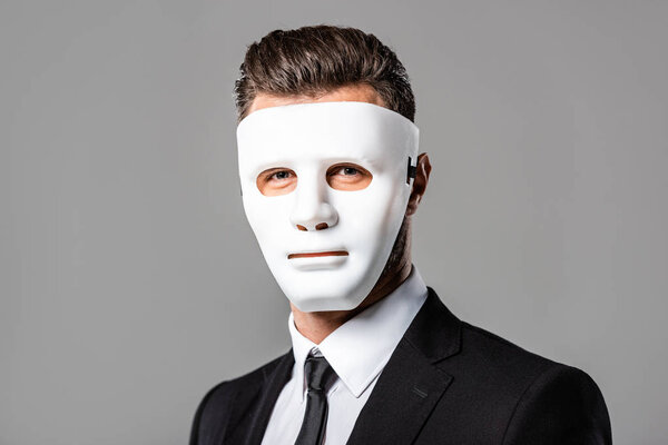 таинственный бизнесмен в черном костюме и маске изолирован на сером
