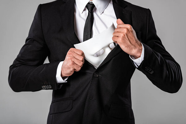 cropped view of businessman in black suit holding white mask isolated on grey
