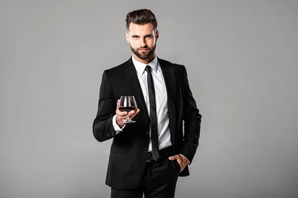 成功的商人在黑色西装拿着玻璃与威士忌隔离在灰色 — 图库照片