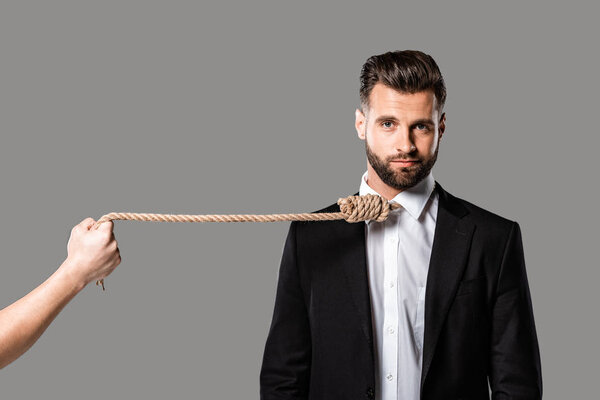 depressed businessman in black suit with noose on neck near murderer with rope isolated on grey