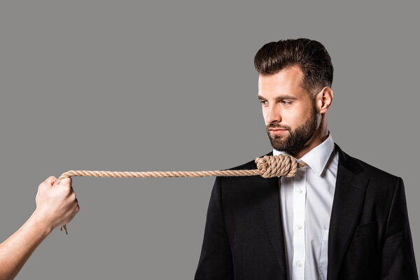 depressed businessman in black suit with noose on neck looking at murderer with rope isolated on grey