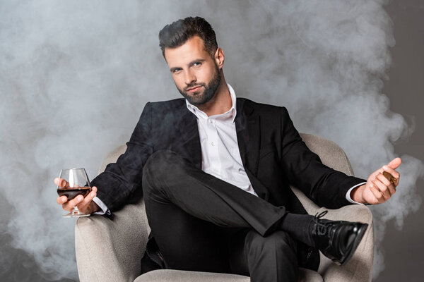 бизнесмен в черном костюме сидит в кресле с сигарой и виски в дыму
