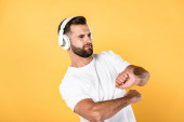handsome man in white t-shirt listening music in headphones and dancing isolated on yellow