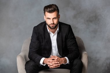 siyah takım elbiseli başarılı işadamı gri arka planda duman içinde koltukta oturan