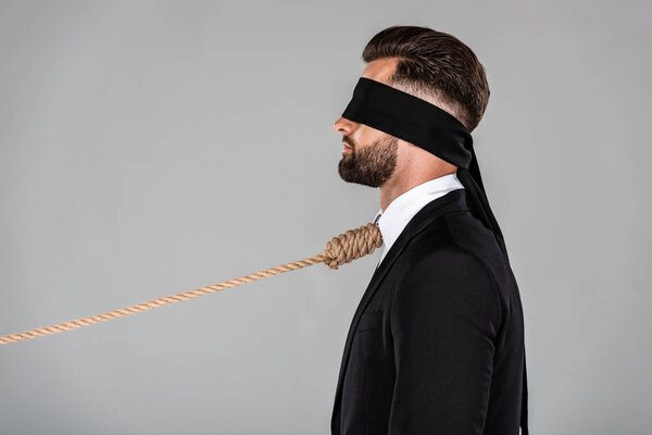 side view of blindfolded businessman in black suit with noose on neck isolated on grey