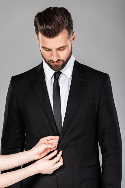 woman fastening button on successful businessman black suit isolated on grey
