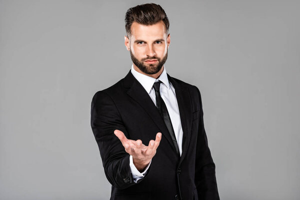 serious businessman in black suit with begging hand isolated on grey