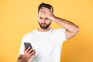upset man in white t-shirt with facepalm using smartphone isolated on yellow clipart