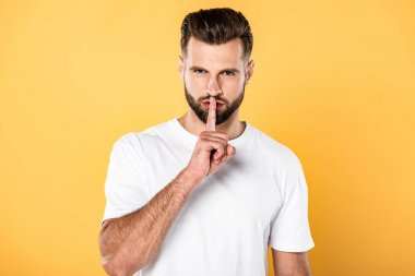 handsome man in white t-shirt showing shh sign isolated on yellow clipart
