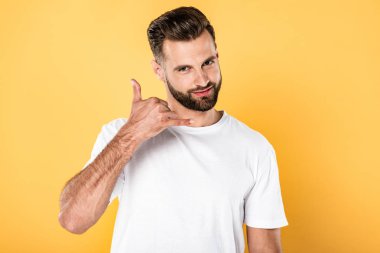smiling handsome man in white t-shirt showing call me gesture isolated on yellow clipart