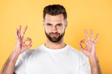 handsome man in white t-shirt showing okay signs isolated on yellow clipart