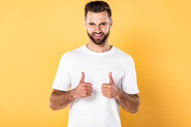 beyaz t-shirt gülümseyen yakışıklı adam kameraya bakarak ve sarı izole başparmak gösteren
