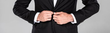 cropped view of elegant businessman in black suit fastening button isolated on grey, panoramic shot clipart