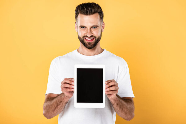 happy man in white t-shirt showing digital tablet with blank screen isolated on yellow