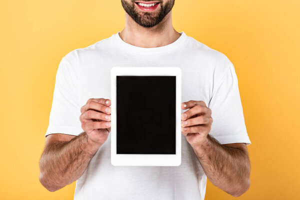 partial view of smiling man in white t-shirt showing digital tablet with blank screen isolated on yellow