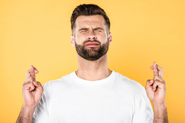 красивый мужчина в белой футболке со скрещенными пальцами, изолированными на желтом
