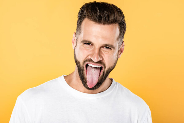 handsome funny man showing tongue isolated on yellow