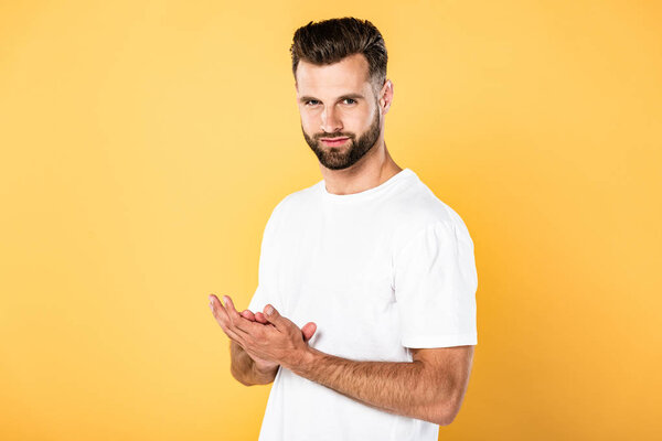 handsome man in white t-shirt rubbing his hands isolated on yellow