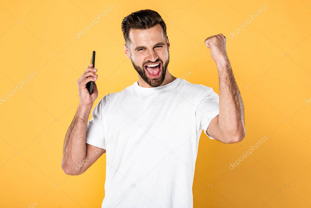 happy man in white t-shirt talking on smartphone and showing yes gesture isolated on yellow
