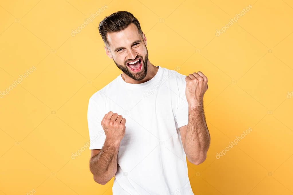 happy man in white t-shirt showing winner gesture isolated on yellow