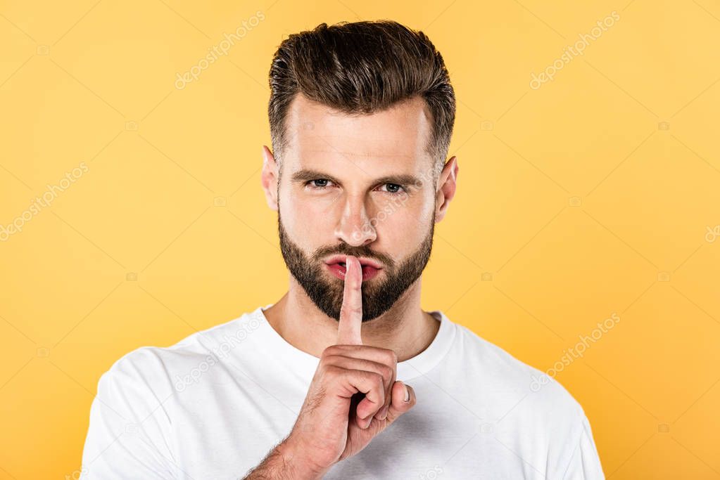 handsome man in white t-shirt showing hush sign isolated on yellow