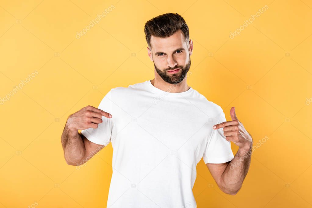 Egotistical handsome man in white t-shirt pointing with fingers at himself isolated on yellow