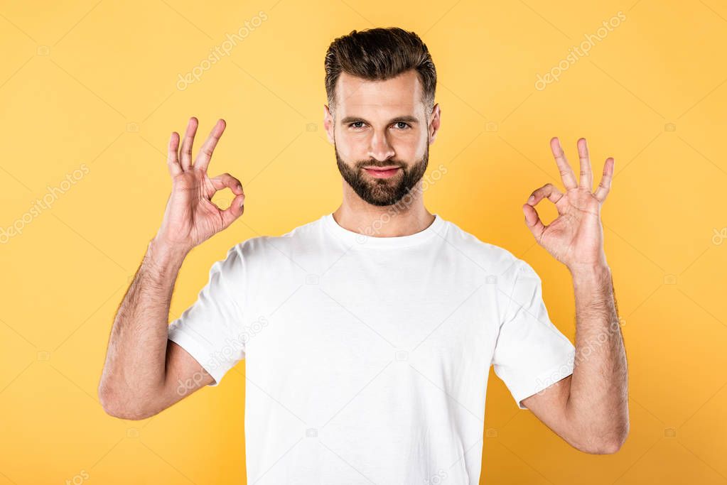 handsome man in white t-shirt showing ok signs isolated on yellow