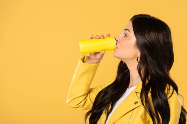 attractive girl drinking soda from can, isolated on yellow  clipart