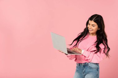 dizüstü bilgisayar kullanarak gülümseyen genç kadın, pembe izole