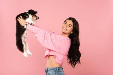 heyecanlı kadın Galce Corgi köpek yavrusu tutan, pembe izole