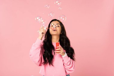 attractive girl blowing soap bubbles isolated on pink clipart