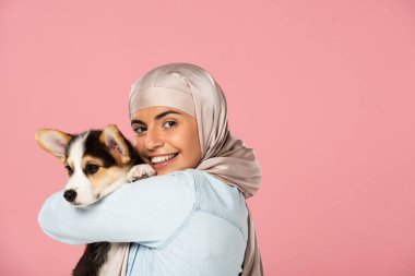 banzamanta gülümseyen müslüman kadın tutarak Corgi köpek yavrusu, pembe izole