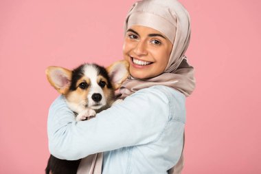 türban gülümseyen müslüman kadın tutarak Galce Corgi köpek yavrusu, pembe izole