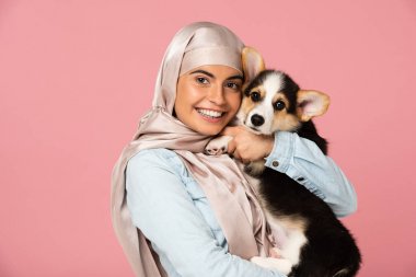 türban gülümseyen arap kız galce Corgi köpek yavrusu tutan, pembe izole