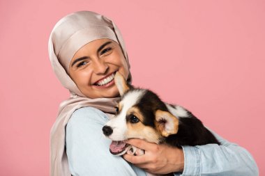 hijab tutan corgi köpek yavrusu gülümseyen arap kız, pembe izole