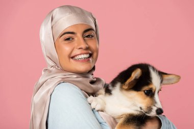 türban mutlu arap genç kadın sevimli corgi köpek yavrusu tutan, pembe izole